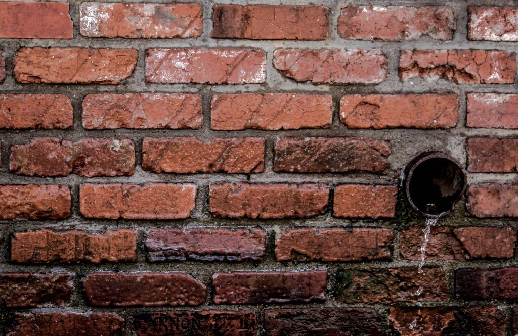 Pexels photo 756901 756901 Close-up of a red brick wall with water flowing from a drain, showcasing texture and patterns.