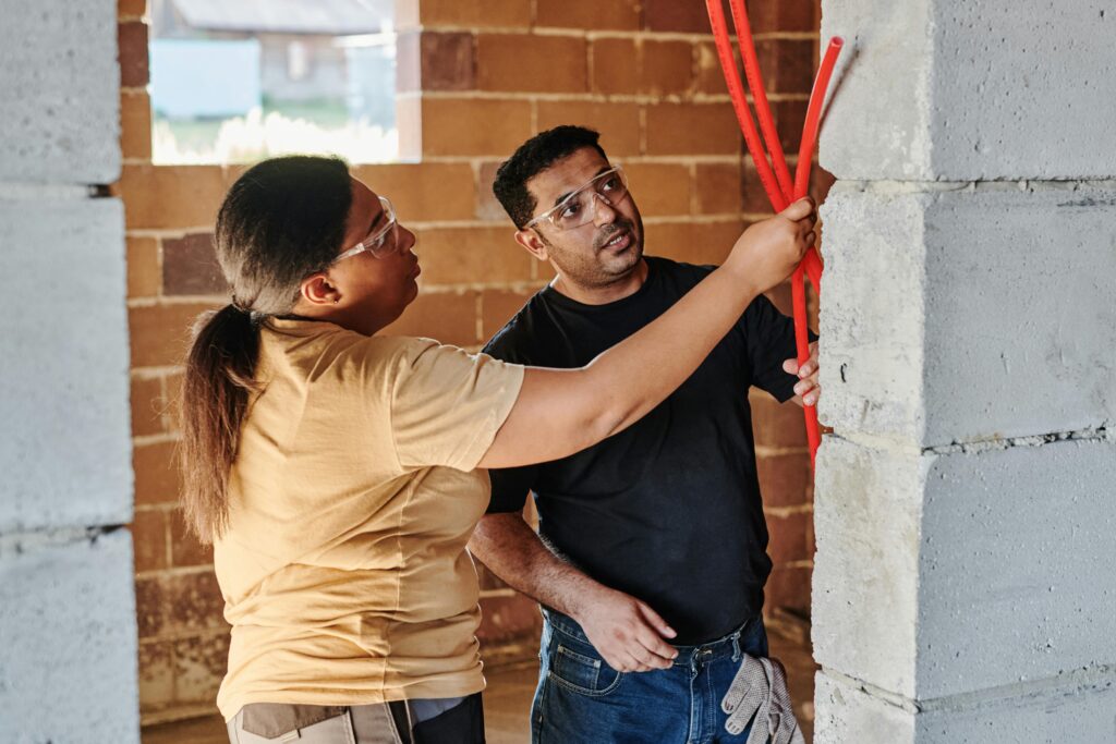 Pexels photo 8961701 8961701 Two construction workers assessing electrical wiring in a brick structure.