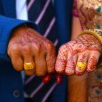Pricing 1 Close-up of bride and groom's hands with intricate mehndi and gold jewelry at an indian wedding.