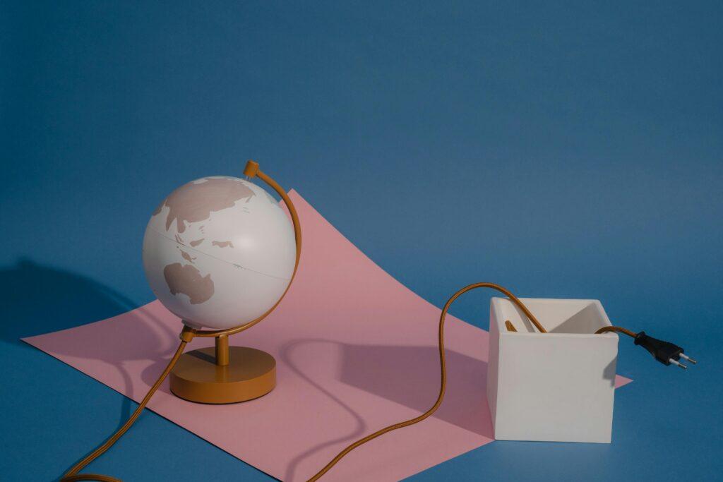 Stylish composition with a globe, pink paper, and box on a blue background.