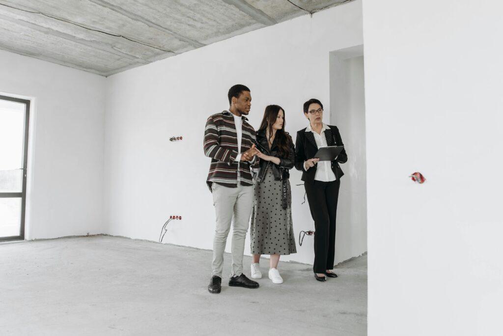 Real estate agent with clients exploring an unfinished apartment interior.